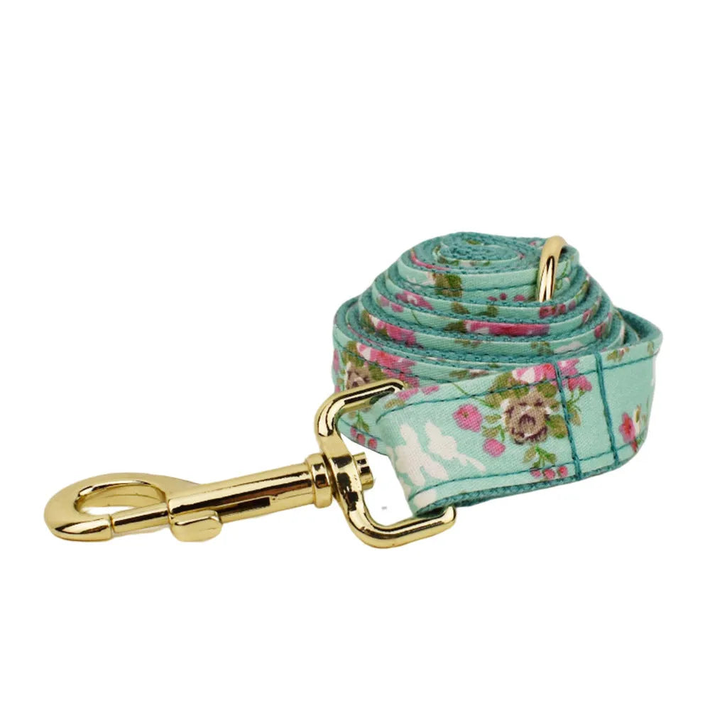 Cloth dog collar with green background and detachable cute bow next to matching leash and vest on a white surface