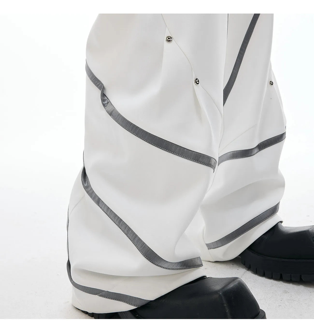 Men's black trousers with metal striped rivet details, pleated front, and a structured three-dimensional cut.