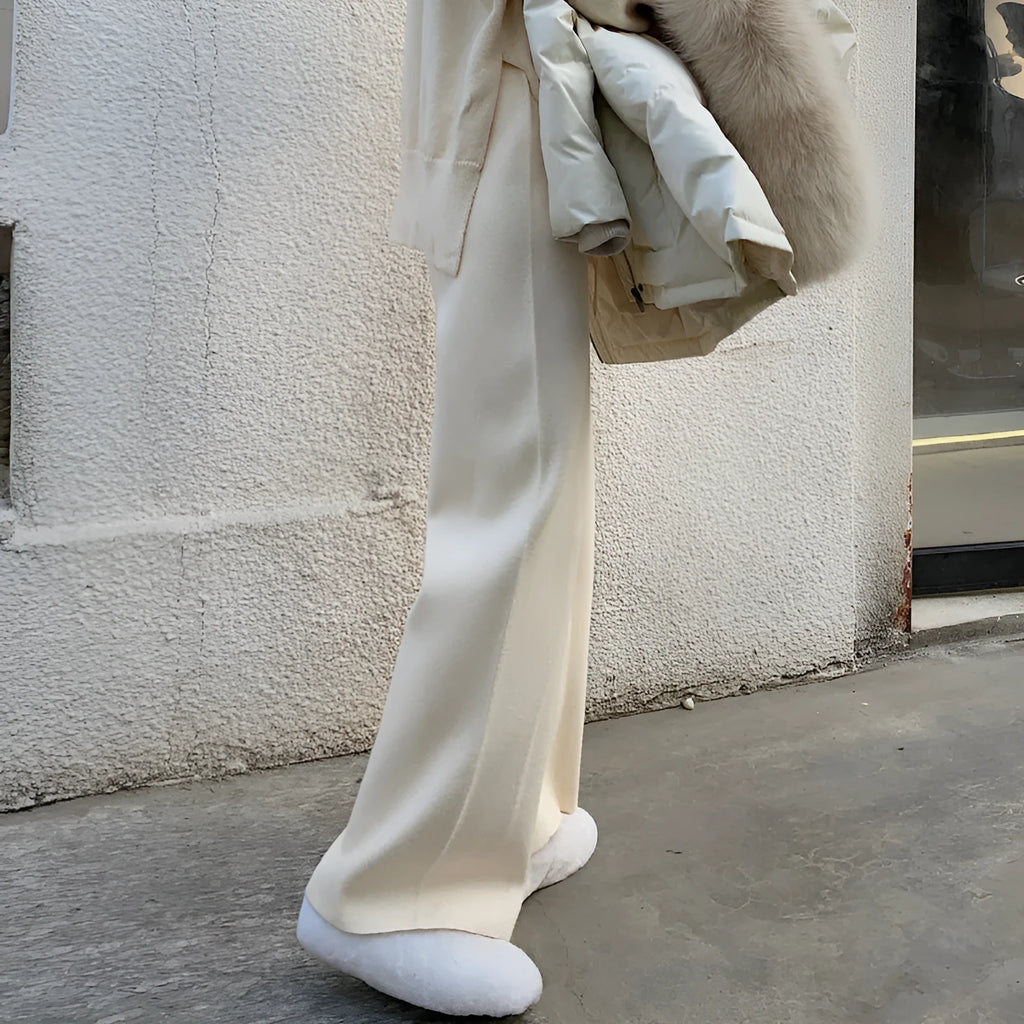 Woman wearing cream white high-waisted knitted wide-leg pants with a drooping mopping silhouette.