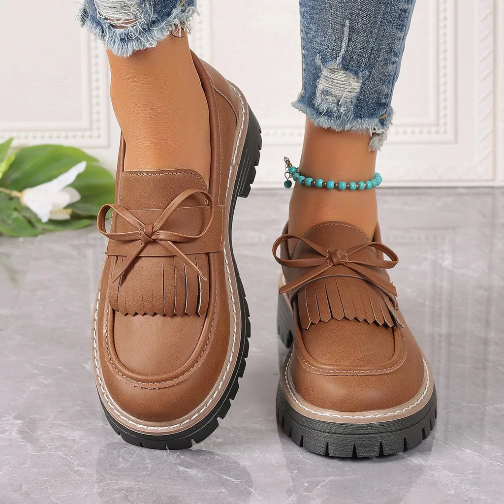 Black plus size women's loafers with a tassel and bowknot detail on the front and a chunky rubber sole.