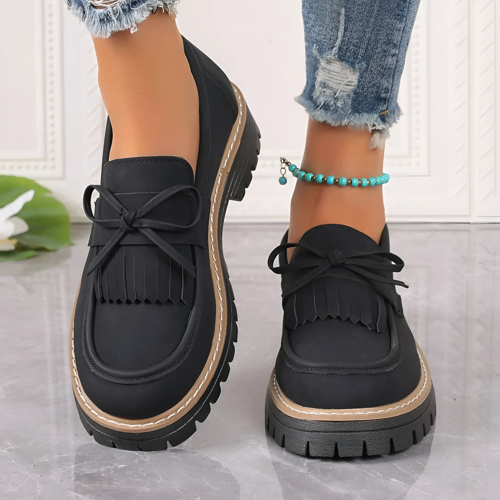 Black plus size women's loafers with a tassel and bowknot detail on the front and a chunky rubber sole.