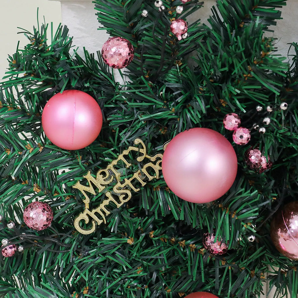Long pink rattan Christmas wreath with small fruit decoration, shown draped on a door.