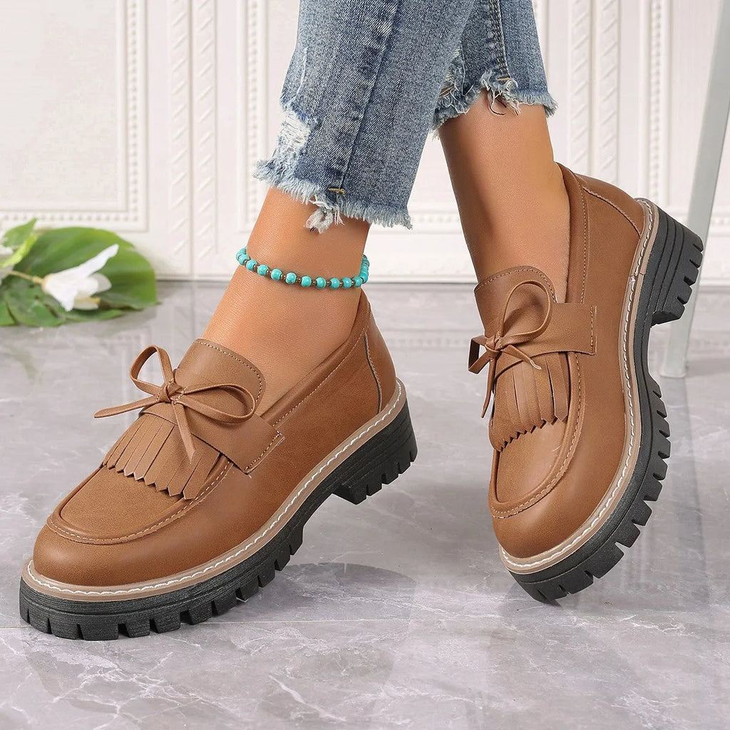 Black plus size women's loafers with a tassel and bowknot detail on the front and a chunky rubber sole.