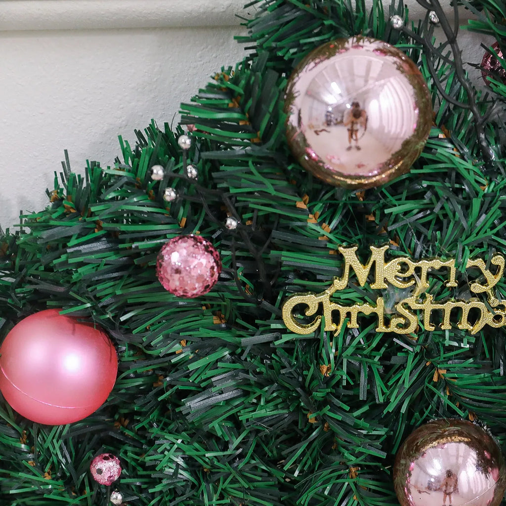 Long pink rattan Christmas wreath with small fruit decoration, shown draped on a door.