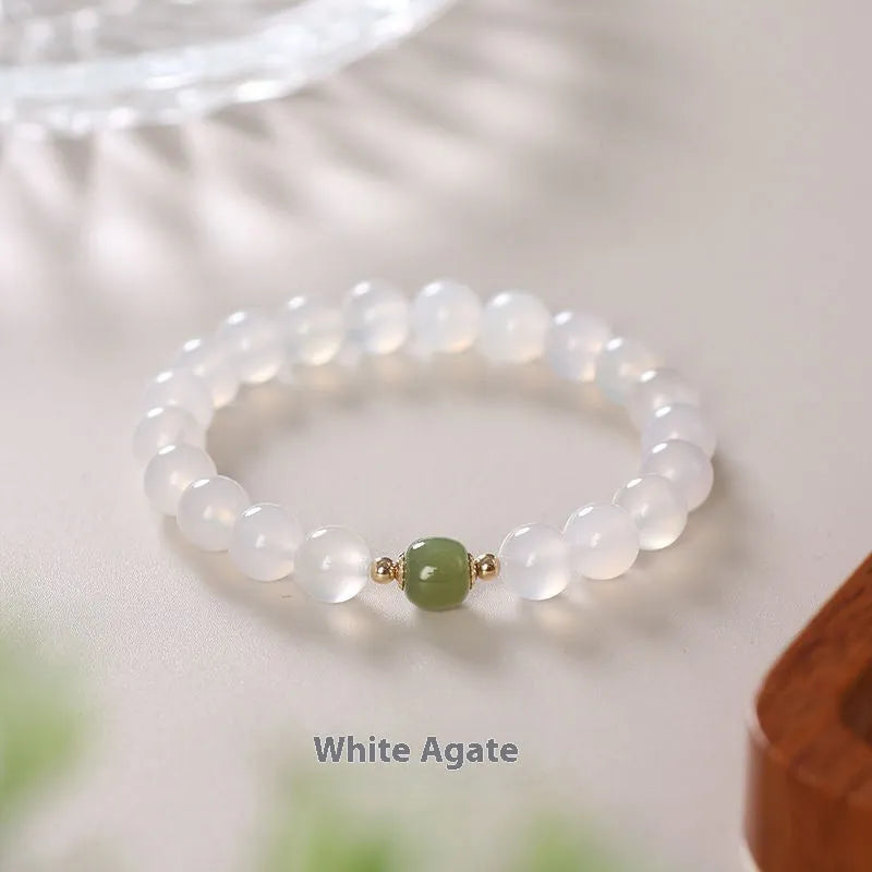 Handmade white agate and cinnabar bracelet with letter charms on a wrist.