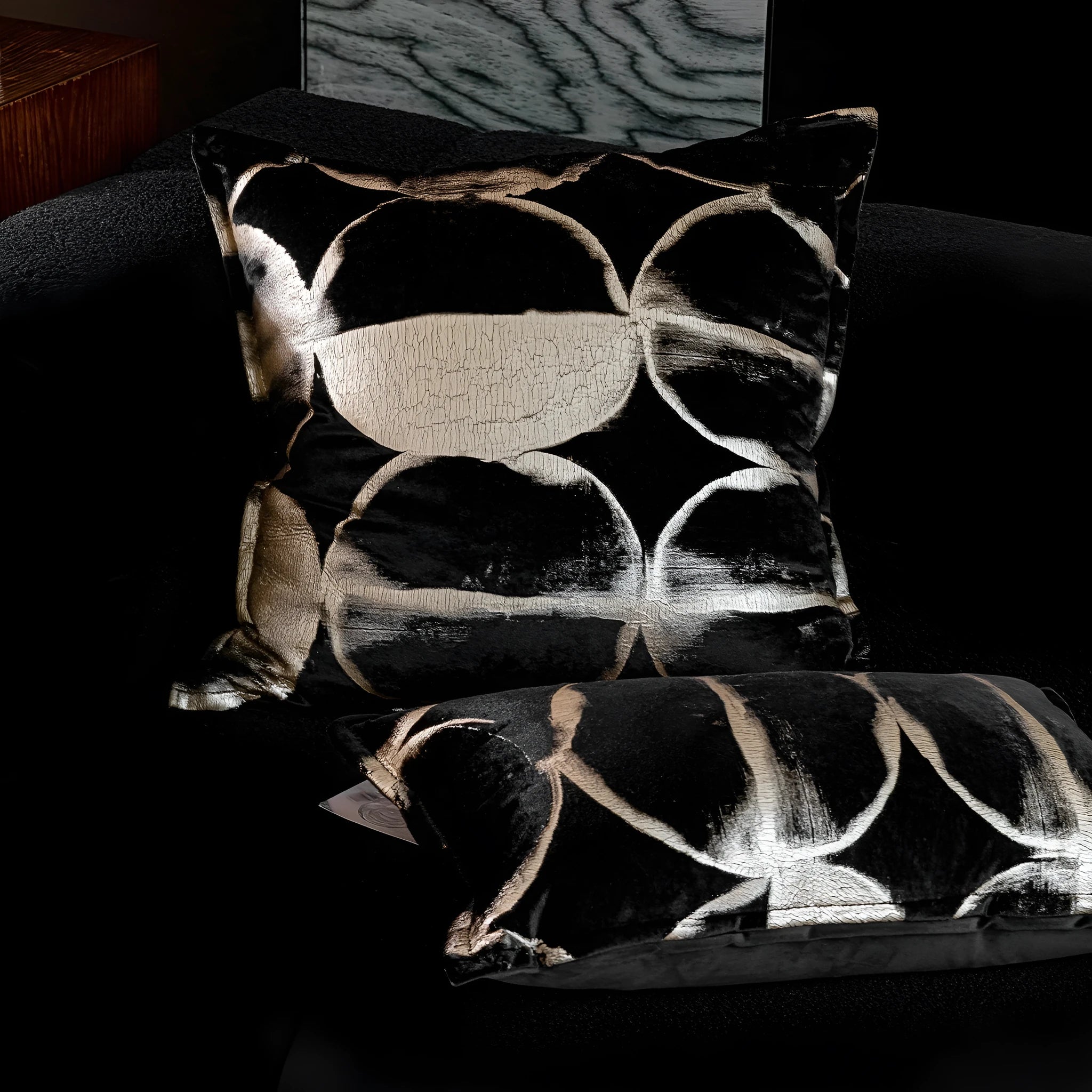 Black and gold abstract patterned decorative flannel cushion on a grey sofa.