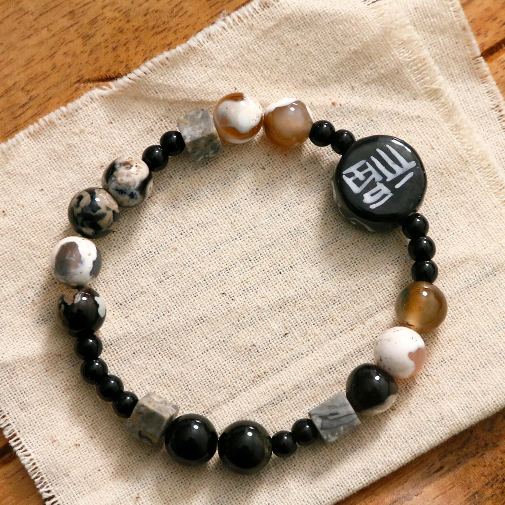 Natural black agate and ceramic round bead hand-woven bracelet on plain background, unisex original design