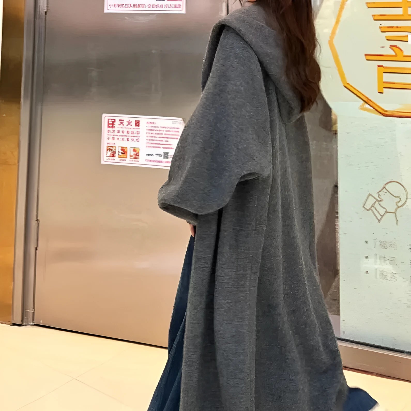 A woman wearing a long, loose, hooded beige knitted cardigan in a Korean casual style.