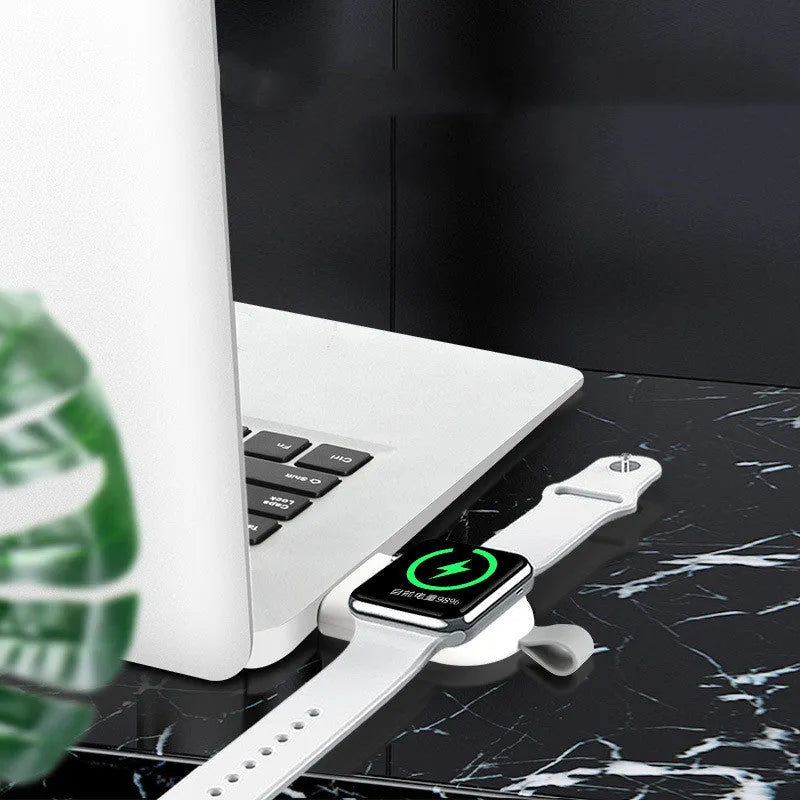 Portable Apple Watch wireless charging dock in white on a wooden table, with USB cable attached.