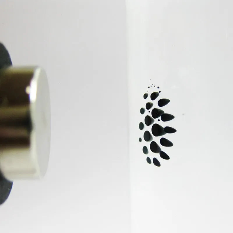 Magnetic fluid toy in a glass bottle with red ferrofluid and two black magnets on a white surface