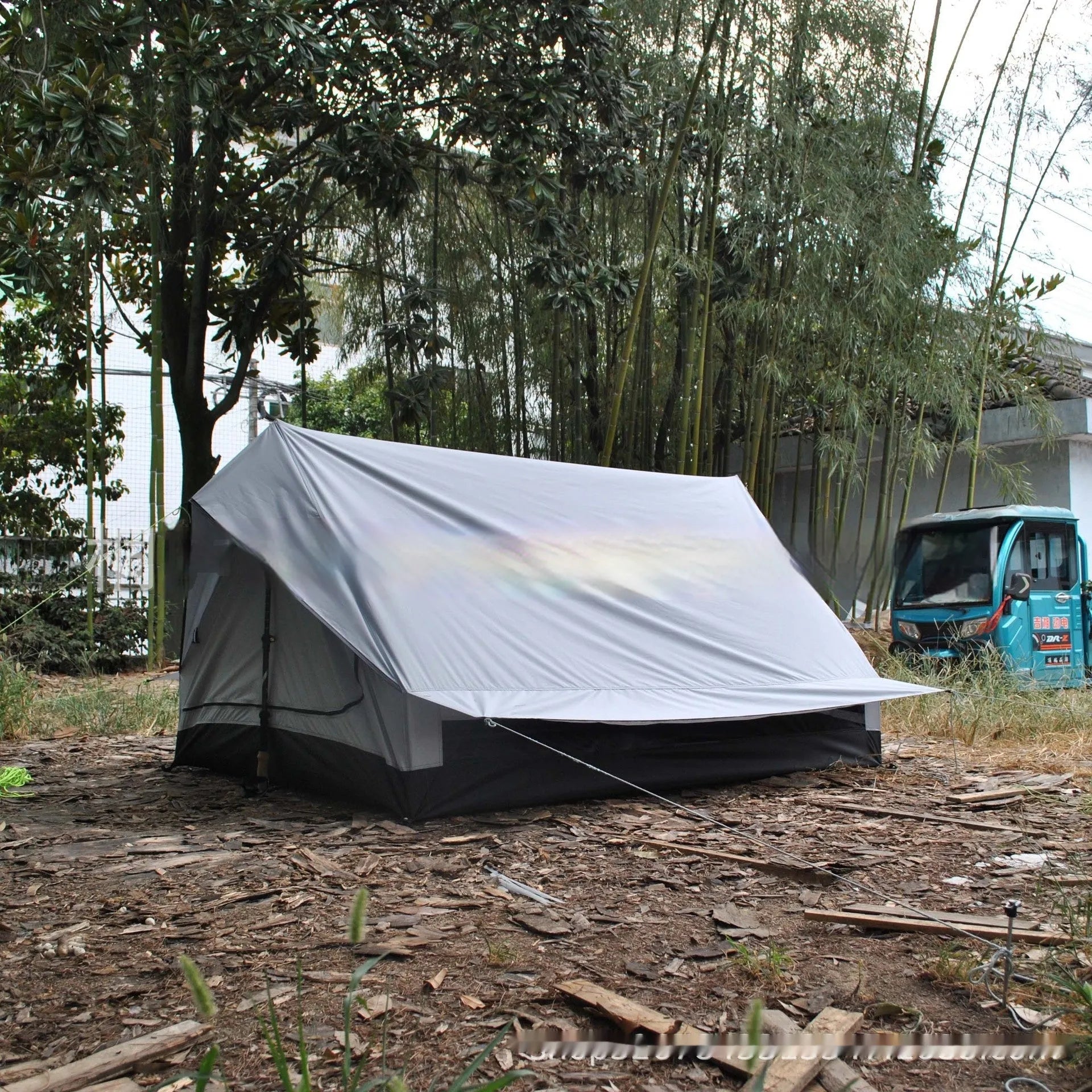Brown A-line hiking tent set up with trekking poles in a forest clearing.