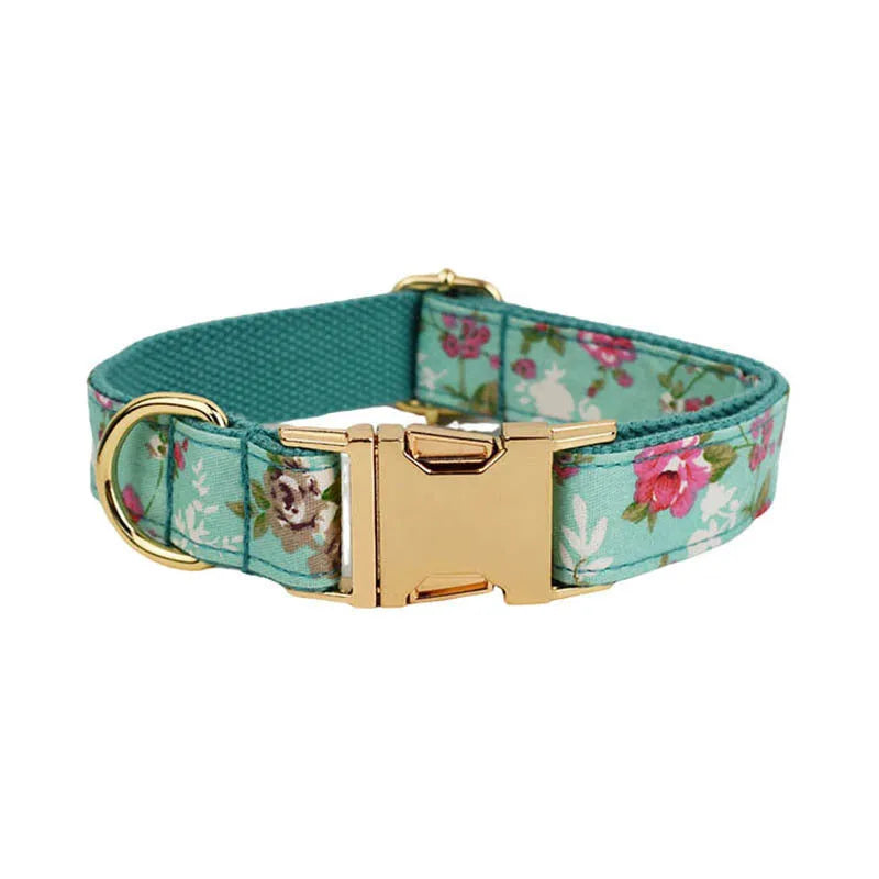 Cloth dog collar with green background and detachable cute bow next to matching leash and vest on a white surface