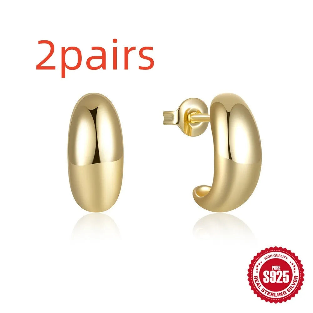 Glossy gold and silver tone C-shaped sterling silver stud earrings on a plain background.