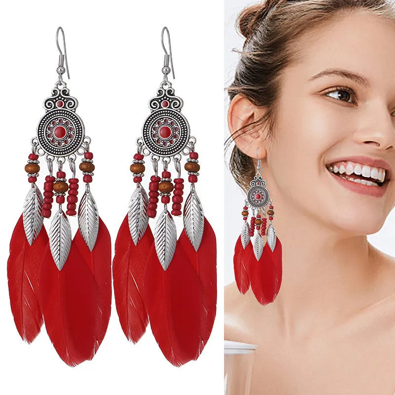 Close-up of a pair of bohemian feather and leaf pattern drop earrings in a light pink electroplated finish.