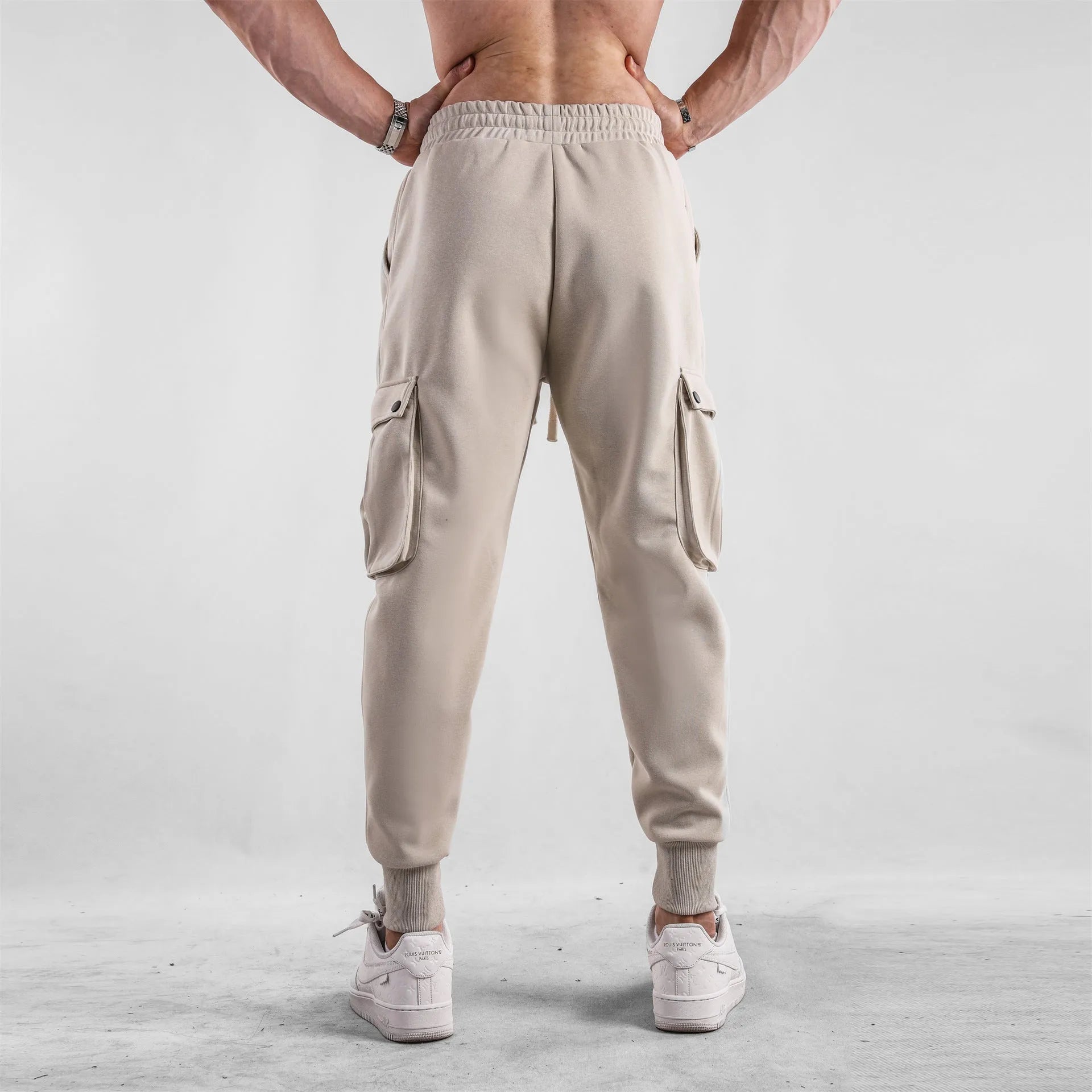 Men's loose fit beige cotton trousers with an ankle tie and multiple pockets on a man standing casually.