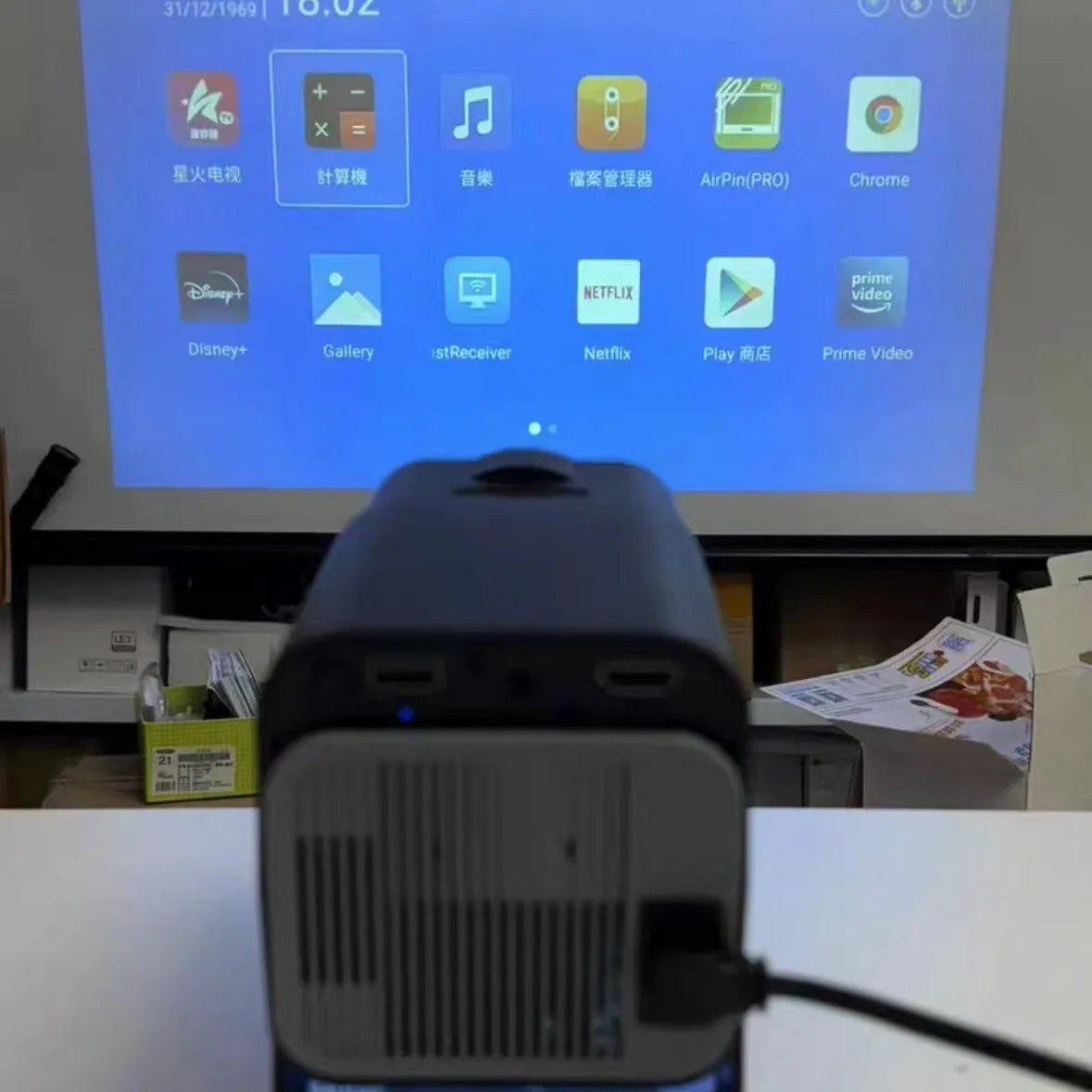 A wireless home projector with a carrying handle, displaying a bright game or movie on a wall.