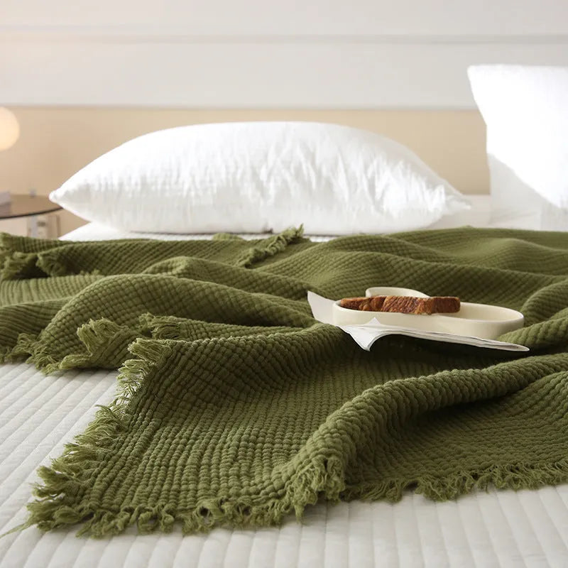 Four-layer gauze tassel cotton blanket in avocado green colour laid flat.