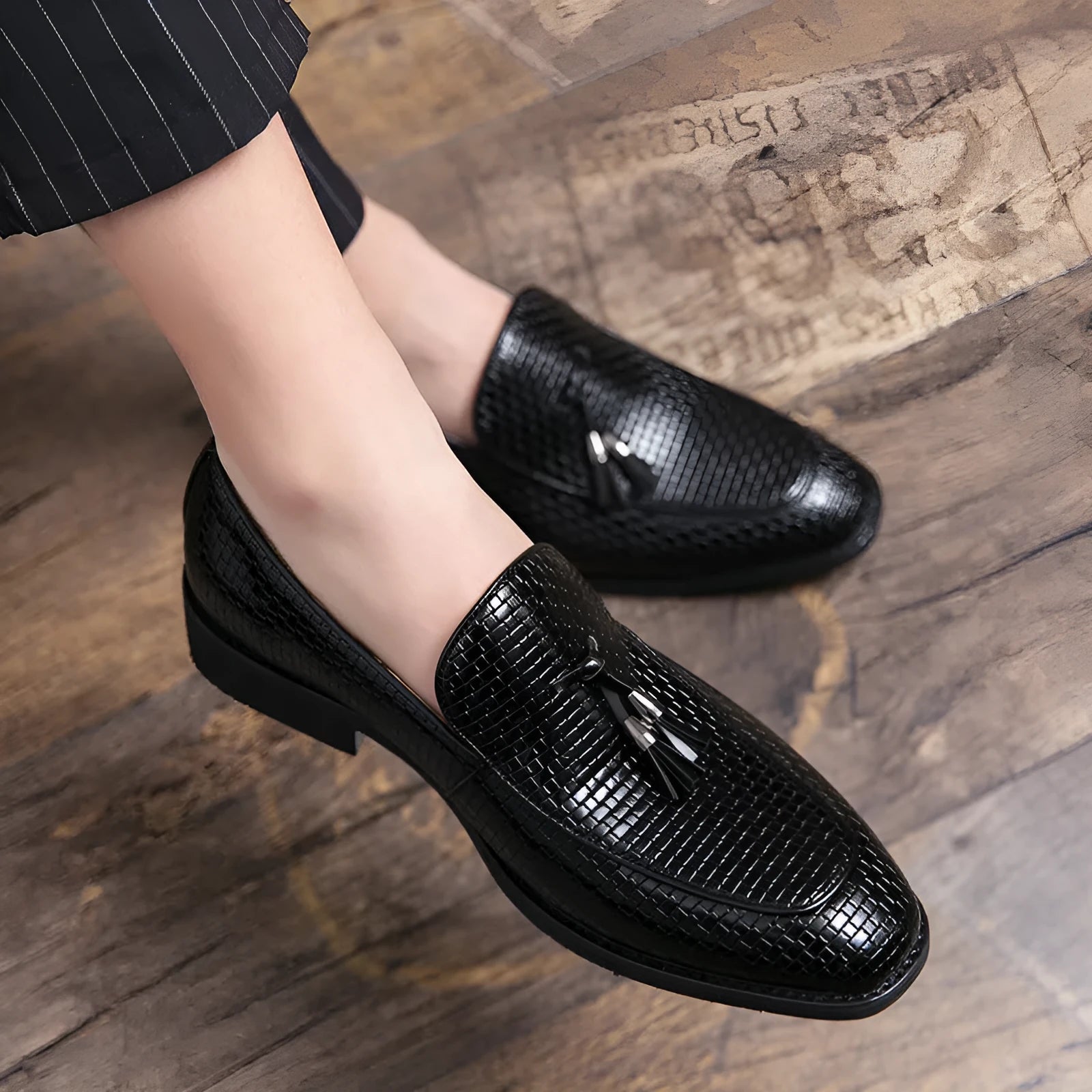 Men's black pointed toe slip-on shoes with a decorative tassel on the front.