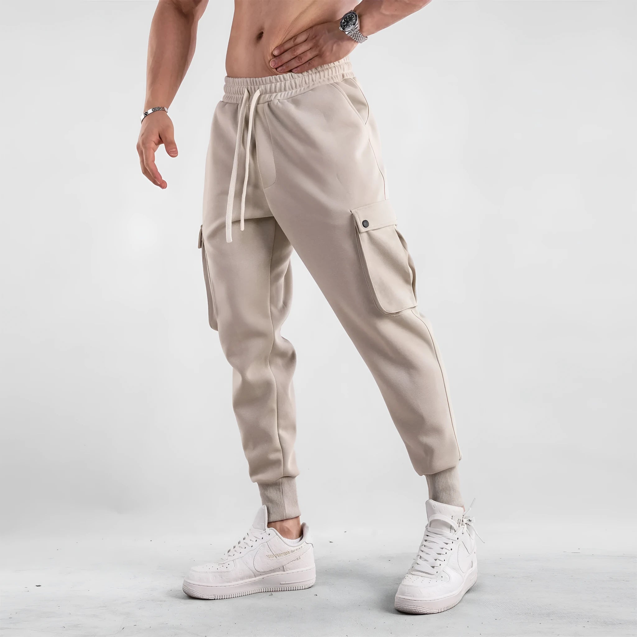 Men's loose fit beige cotton trousers with an ankle tie and multiple pockets on a man standing casually.