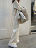 Woman wearing cream white high-waisted knitted wide-leg pants with a drooping mopping silhouette.