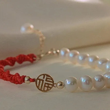 Women's pearl braided red rope bracelet with 14K gold plated fu character charm in geometric shape on white background