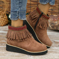 Women's ankle boot in suede with wedge heel, side zipper, and tassel detail on a dark background.