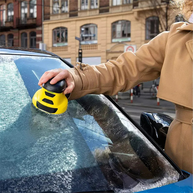 Yellow cordless electric car ice scraper with USB charging cable on a car windshield.