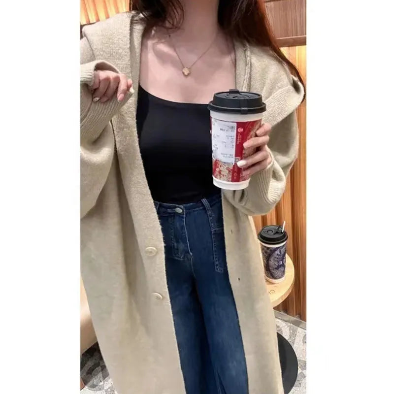 A woman wearing a long, loose, hooded beige knitted cardigan in a Korean casual style.