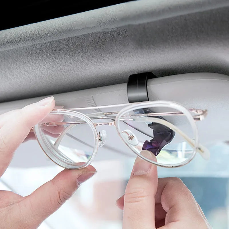 Black plastic clip for car sunshade holding a ticket and glasses