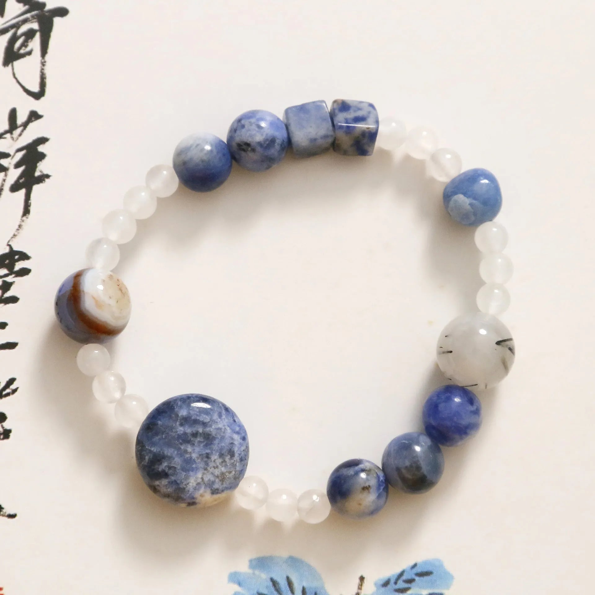 Natural blue point stone and black hair crystal agate hand-woven unisex bracelet with round and oval beads on white background