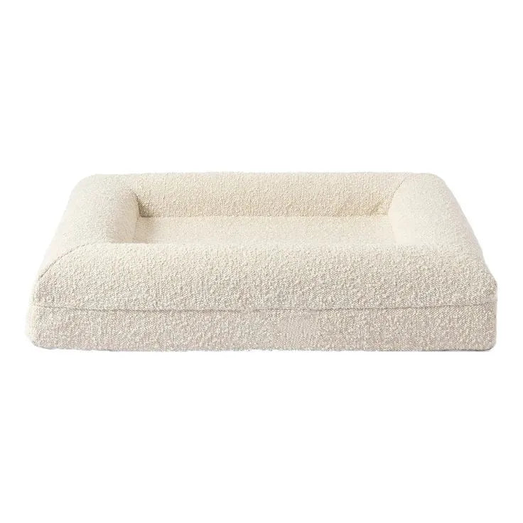 Rectangular beige cloth dog bed nest with raised sides on a plain floor, size M shown