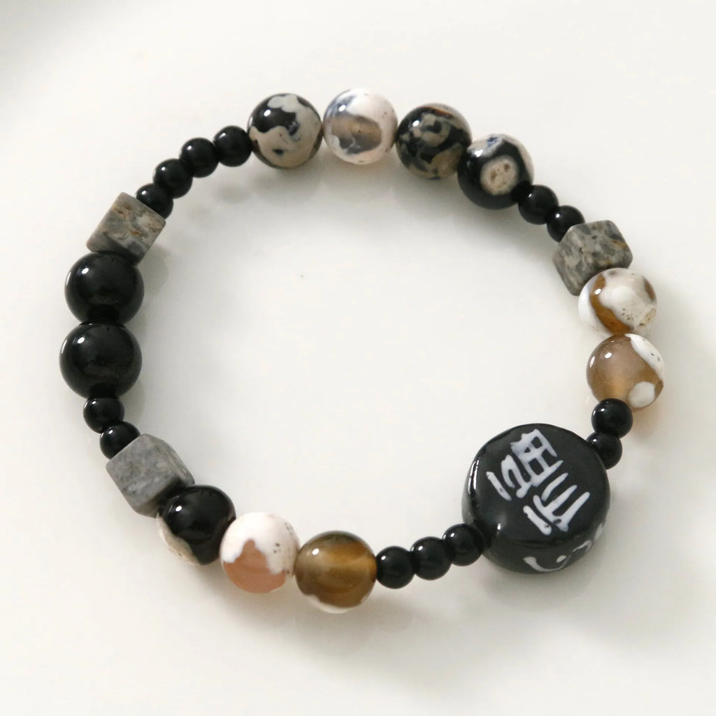 Natural black agate and ceramic round bead hand-woven bracelet on plain background, unisex original design