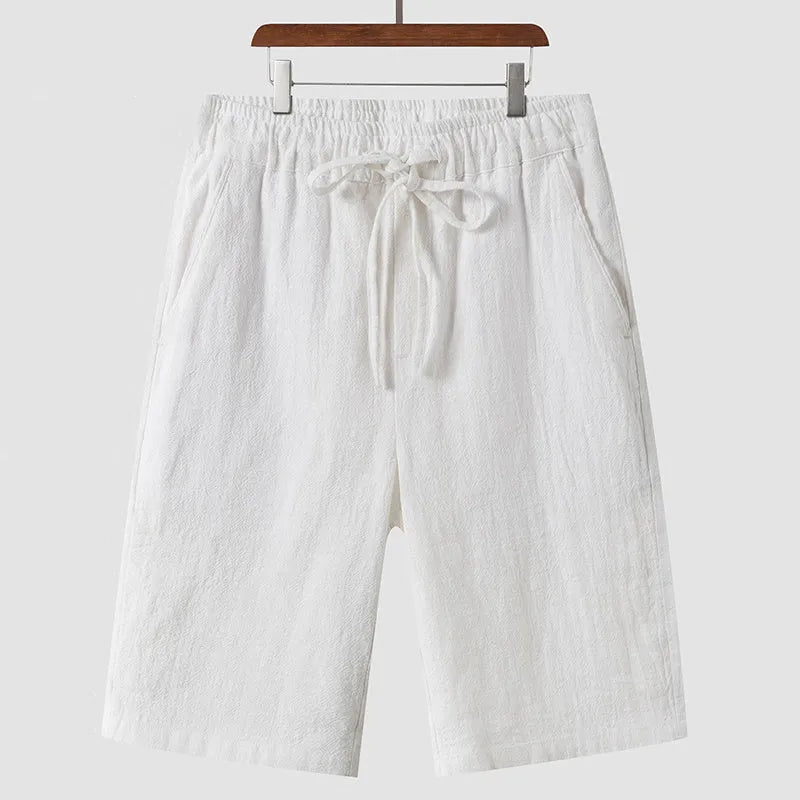 Man wearing beige linen shorts with a loose cropped fit and elasticated mid waist.