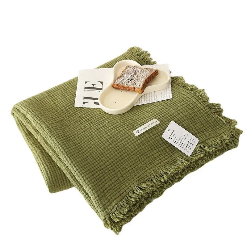 Four-layer gauze tassel cotton blanket in avocado green colour laid flat.