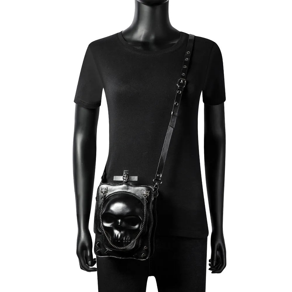 Black mini square crossbody bag with embossed skull design, chain accents, and zipper closure
