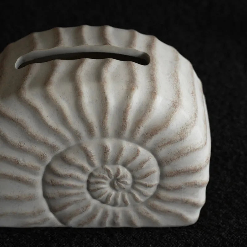 White conch shell shaped resin cover for a rectangular tissue box with a slot for tissue dispensing.