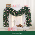 Long pink rattan Christmas wreath with small fruit decoration, shown draped on a door.