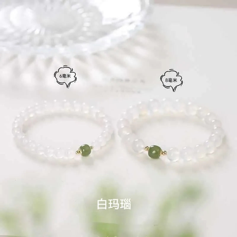 Handmade white agate and cinnabar bracelet with letter charms on a wrist.