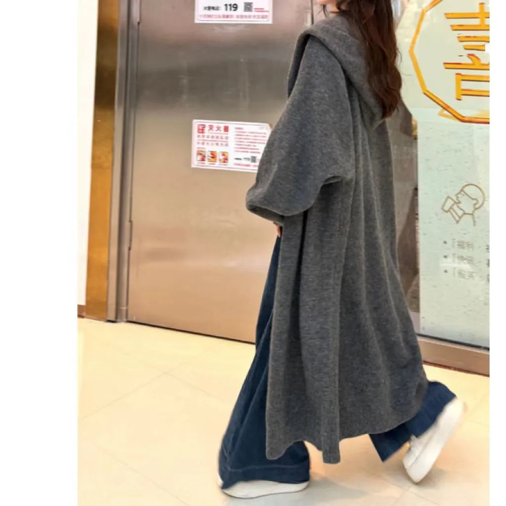 A woman wearing a long, loose, hooded beige knitted cardigan in a Korean casual style.
