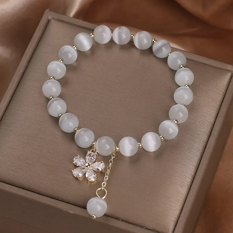 Close-up of a white cat's eye crystal bracelet with a flower tassel pendant and a morganite safety buckle.