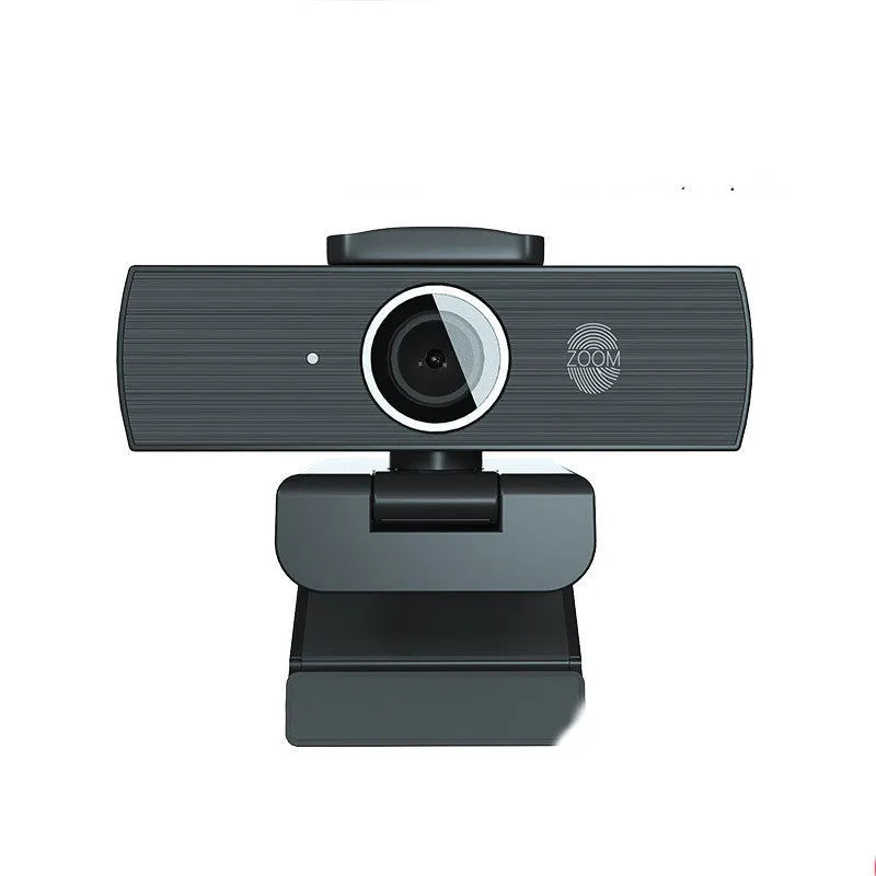 Black USB computer webcam with magnetic privacy cover on a desk next to a laptop.