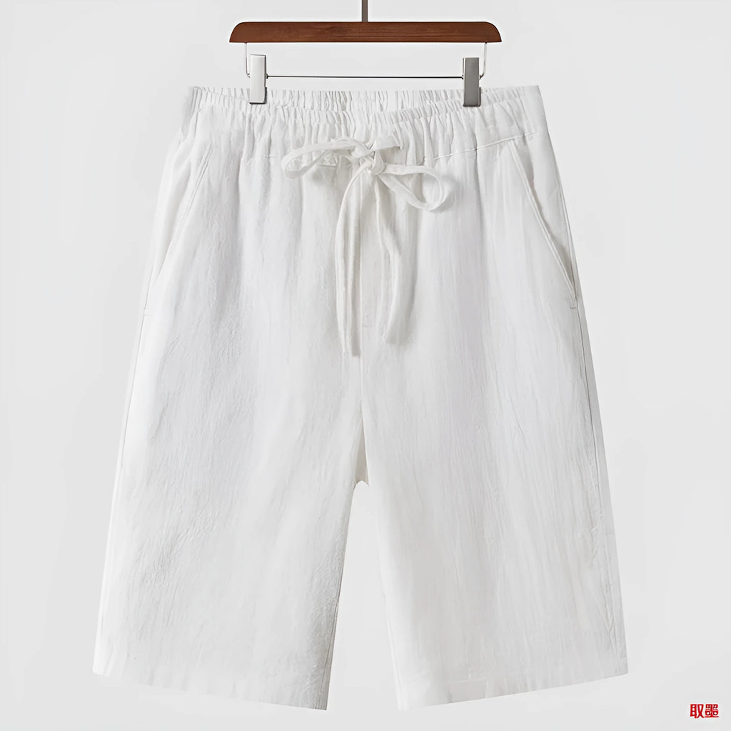 Man wearing beige linen shorts with a loose cropped fit and elasticated mid waist.