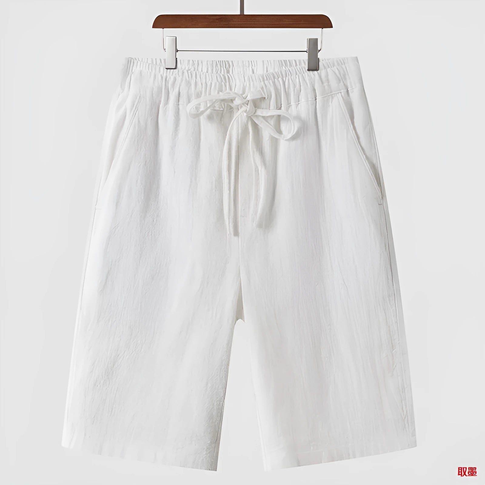 Man wearing beige linen shorts with a loose cropped fit and elasticated mid waist.