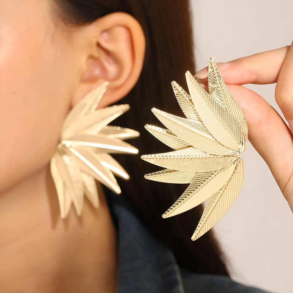 Gold and white leaf-shaped patch earrings made of alloy metal on a neutral background