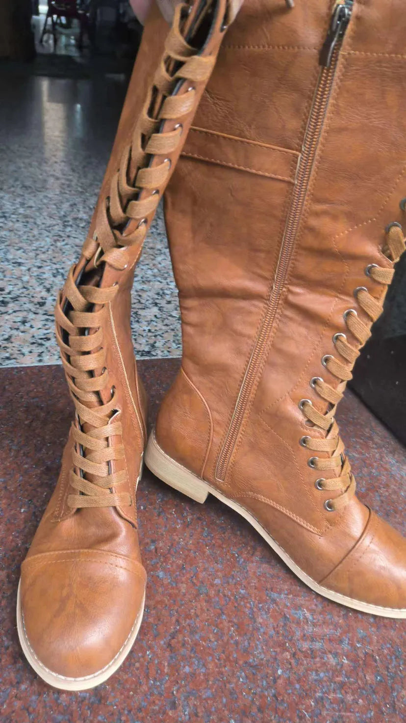 Women's black cross strap knight ankle boots with front laces and side buckle on a solid colour background.
