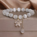 Close-up of a white cat's eye crystal bracelet with a flower tassel pendant and a morganite safety buckle.
