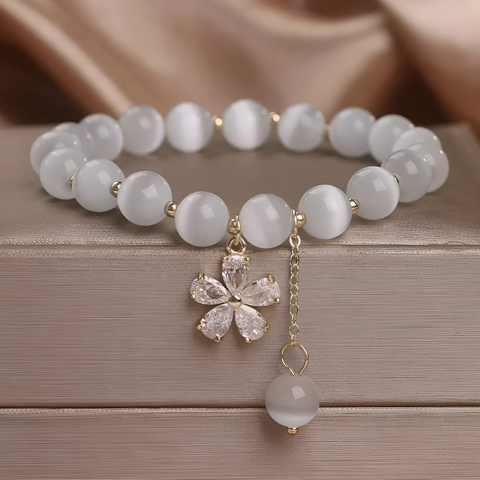 Close-up of a white cat's eye crystal bracelet with a flower tassel pendant and a morganite safety buckle.