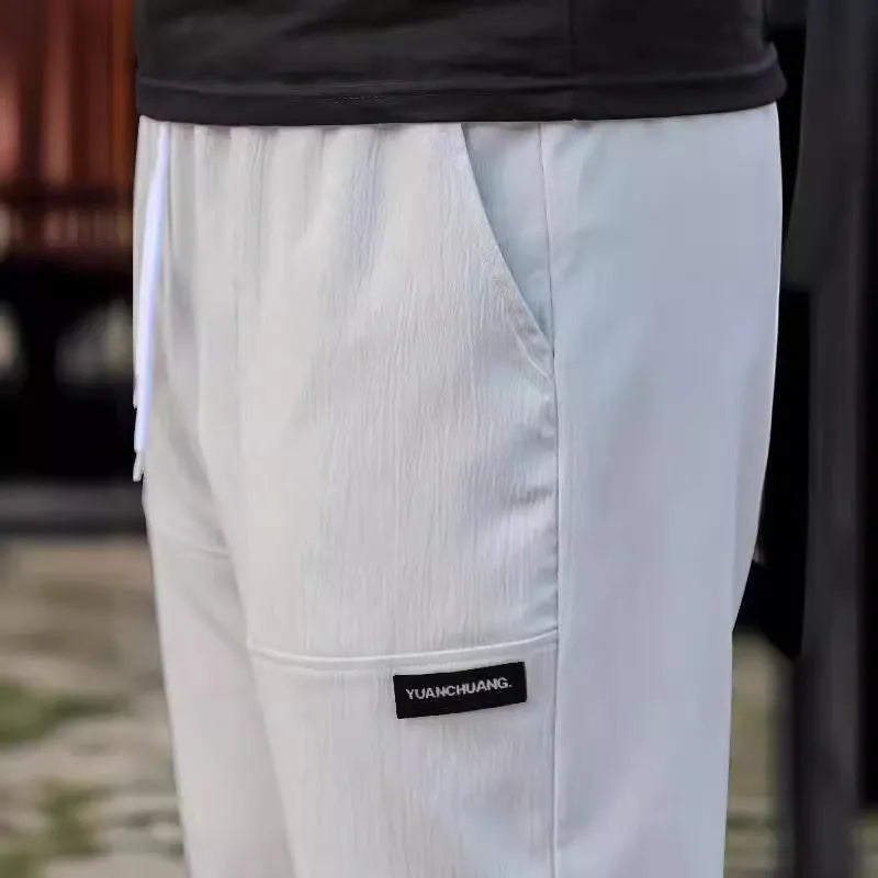 Men's polyester trousers in light grey, shown folded, for casual spring and autumn wear.