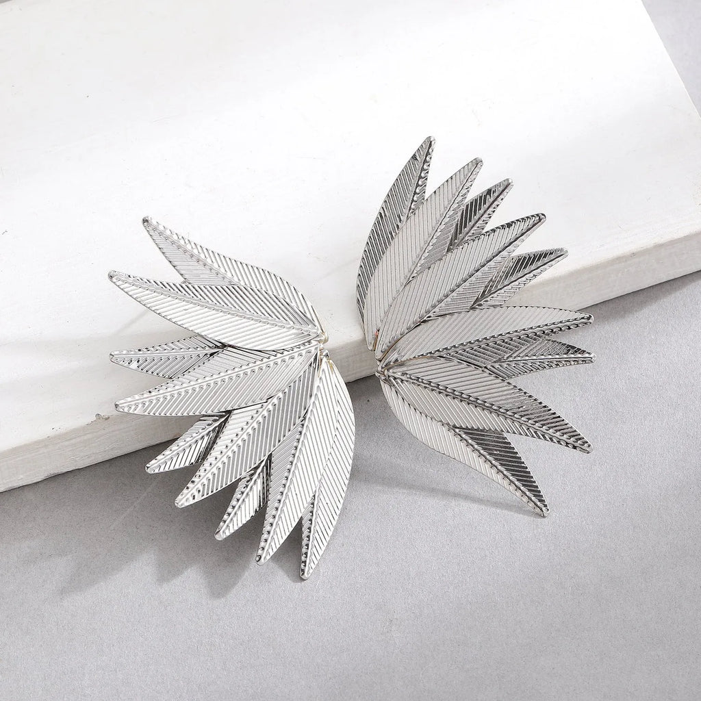 Gold and white leaf-shaped patch earrings made of alloy metal on a neutral background