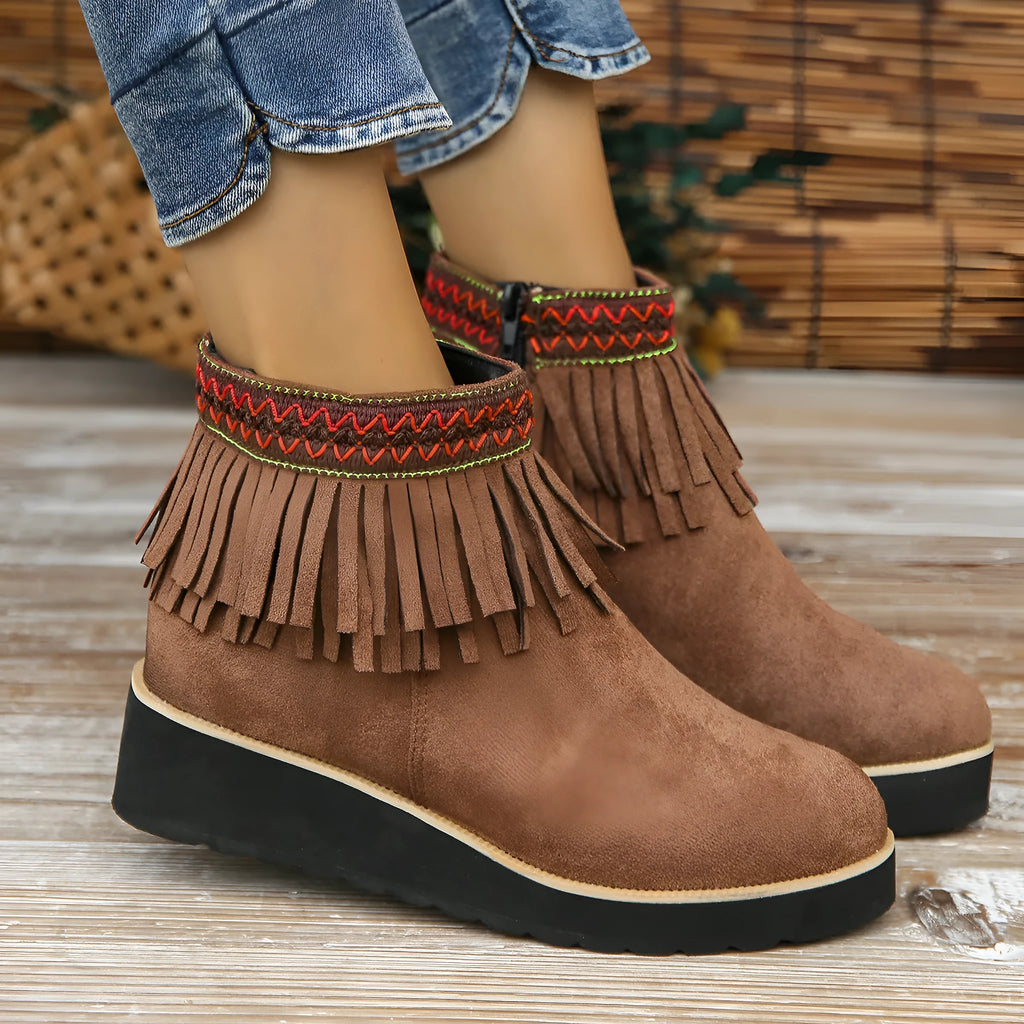 Women's ankle boot in suede with wedge heel, side zipper, and tassel detail on a dark background.